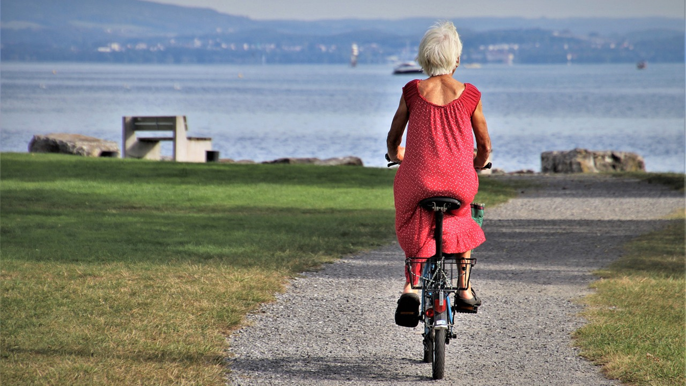 Mujer mayor paseando en bicicleta junto al mar