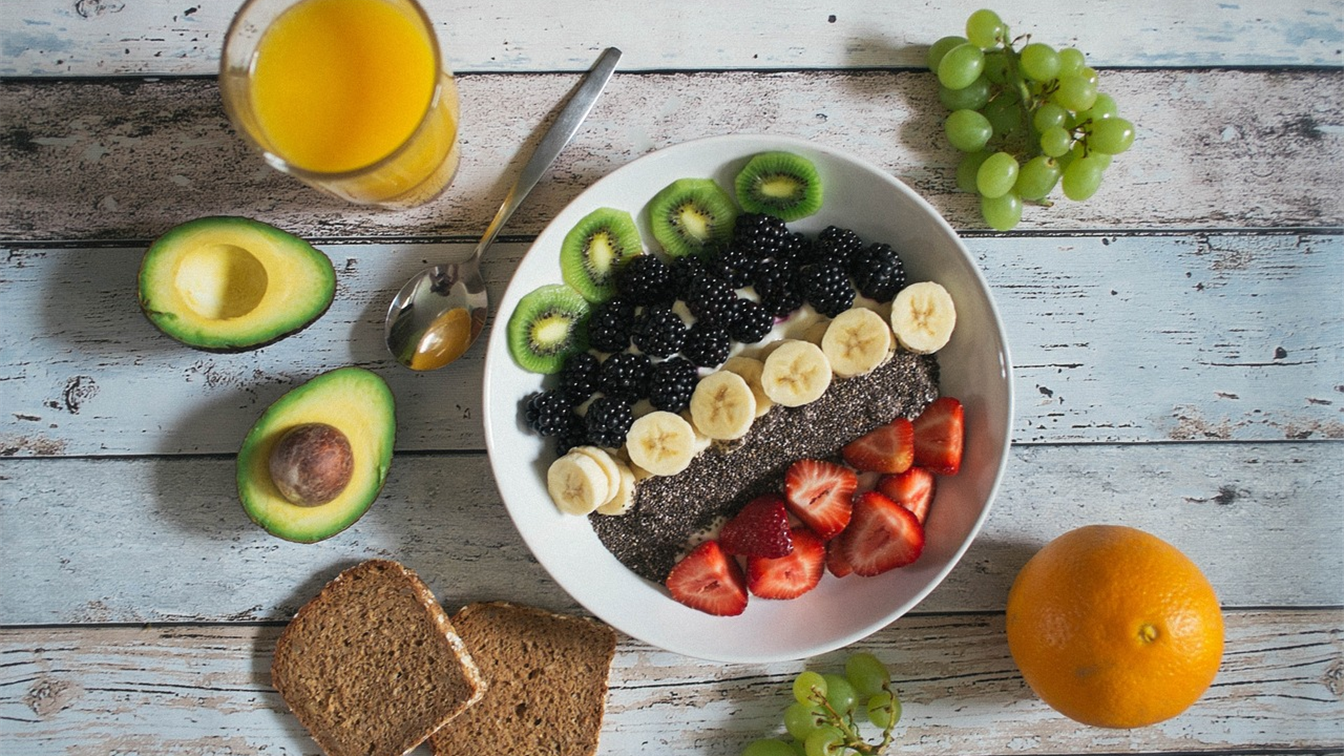 Bol de fruta fresca con kiwi, moras, plátano y fresas junto a aguacate y pan integral