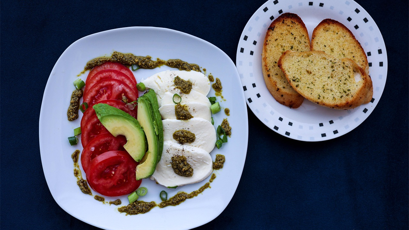 Plato de tomate, aguacate y mozzarella con pan tostado sobre una mesa